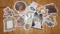 A collection of assorted die-cut stickers featuring various designs, including a dog portrait, a vintage gramophone, a picture frame, and text stickers, arranged on a wooden floor.